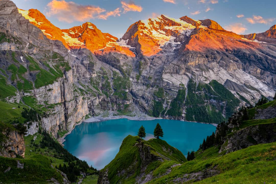 Vista aérea del Oeschinensee al atardecer con el alpenglow tiñendo de naranja y oro las paredes del Blüemlisalp sobre el lago turquesa, Oberland bernés, Suiza