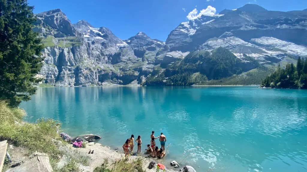 Grupo de bañistas en la orilla del Oeschinensee un día de verano, con todo el lago turquesa y las cumbres del Blüemlisalp al fondo, Kandersteg, Suiza