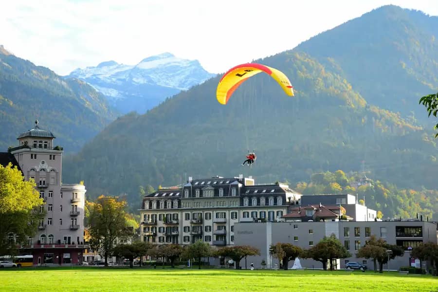 Tandem paraglider landing on Höhematte meadow in central Interlaken with historic hotels and Swiss Alps in autumn