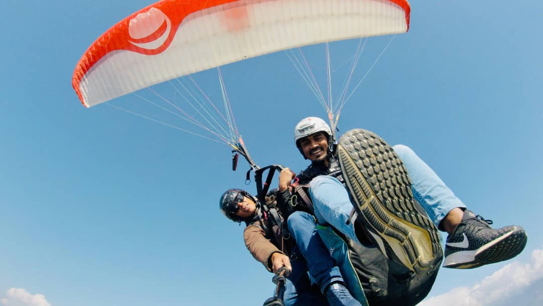 Tandem paragliding pilot and passenger smiling mid-flight above Interlaken Switzerland with red canopy and blue sky
