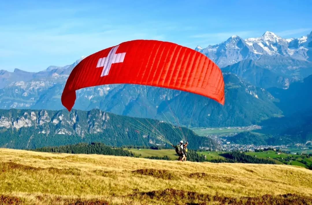 Tandem paragliding takeoff with Swiss flag canopy above Interlaken valley and Jungfrau massif, Bernese Oberland