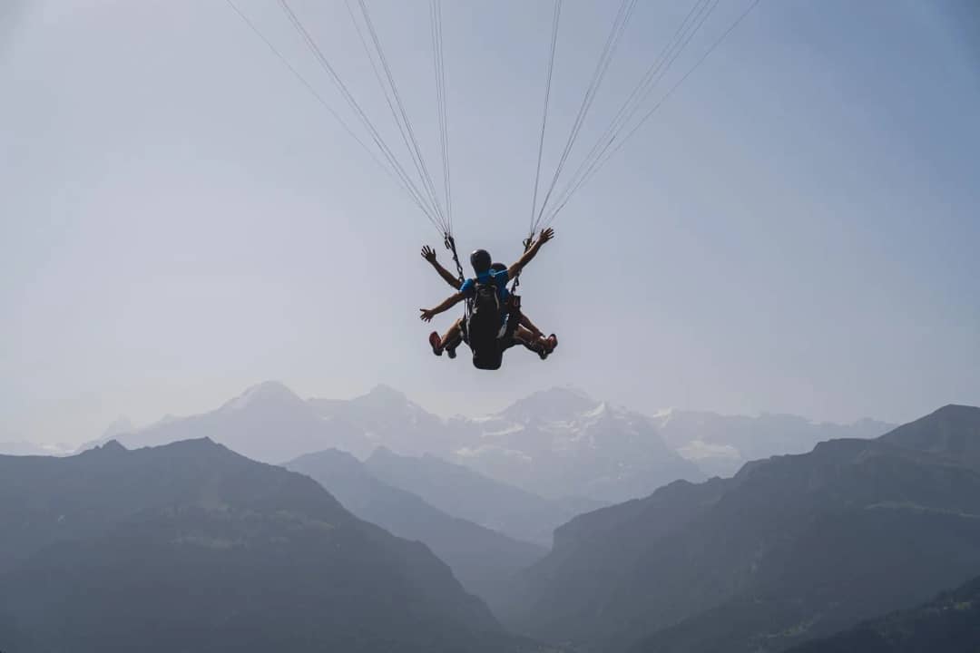 Tandem paragliding passenger with arms wide open above the Swiss Alps near Interlaken, Bernese Oberland valley below