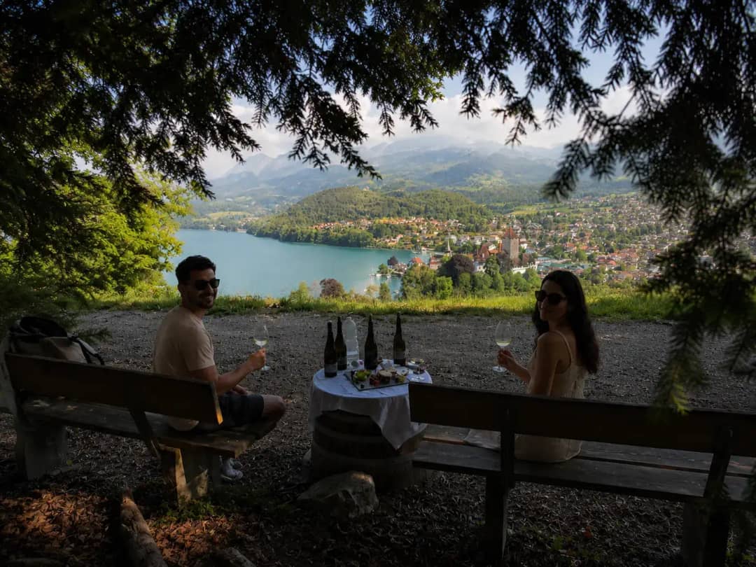 Couple tasting white wine with cheese board above Lake Thun and Spiez village, outdoor intimate wine tasting from Interlaken