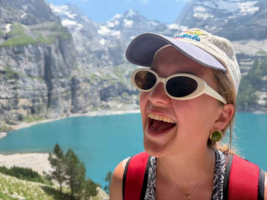 Happy female hiker laughing above turquoise alpine lake with limestone peaks, Swiss Alps Bernese Oberland Switzerland