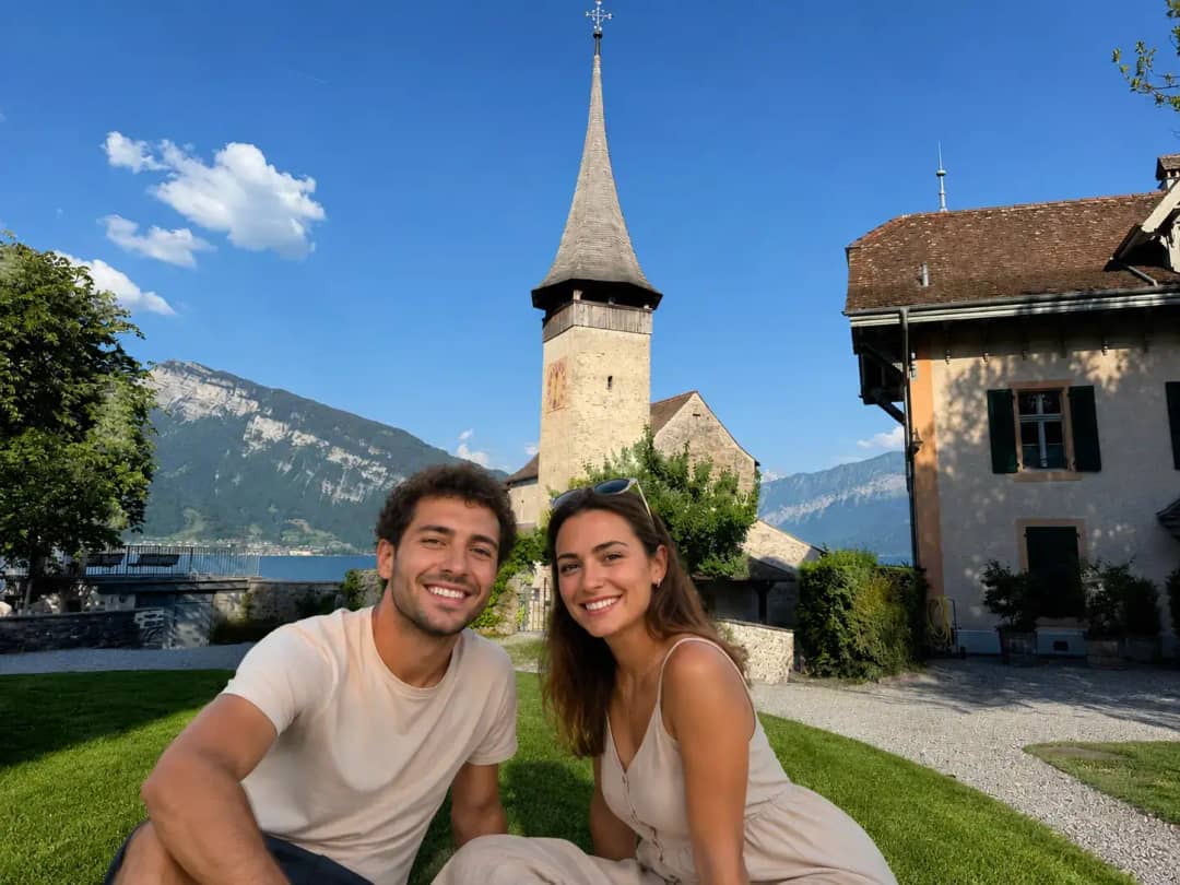 Smiling couple on the grass by the Spiez Castle church tower above Lake Thun
