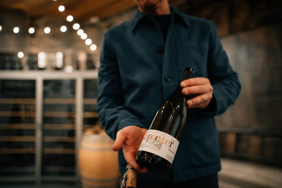 Winemaker holding a bottle of Spiezer Blauburgunder in a candle-lit cellar