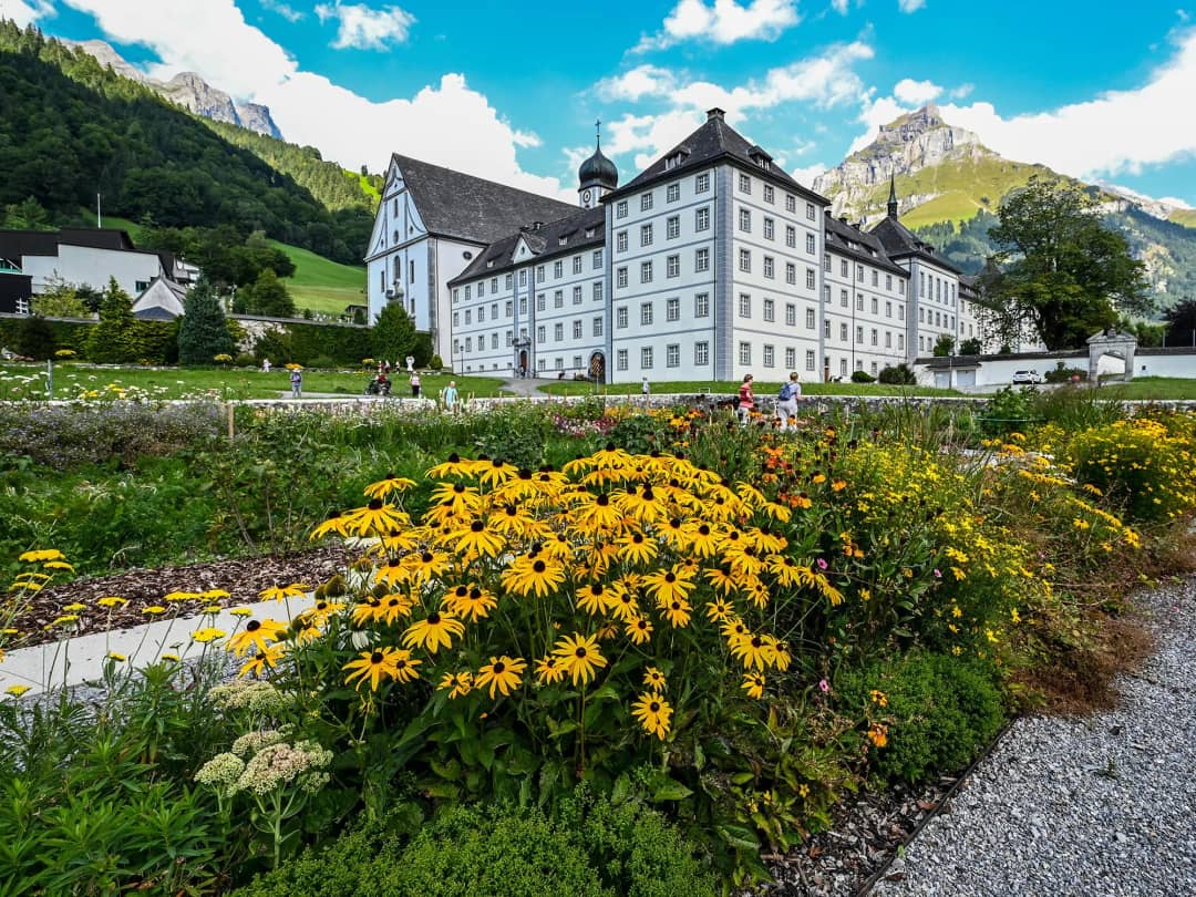 Engelberg Abbey and its show cheese dairy behind summer flower beds, framed by the Swiss Alps