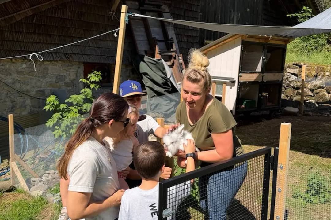 Daniela showing a white rabbit to a family with young children beside the hutches at her alpine farm