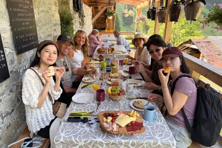 Guests sharing a Swiss farm breakfast of cheese, bread and charcuterie at a long table on the farmhouse terrace