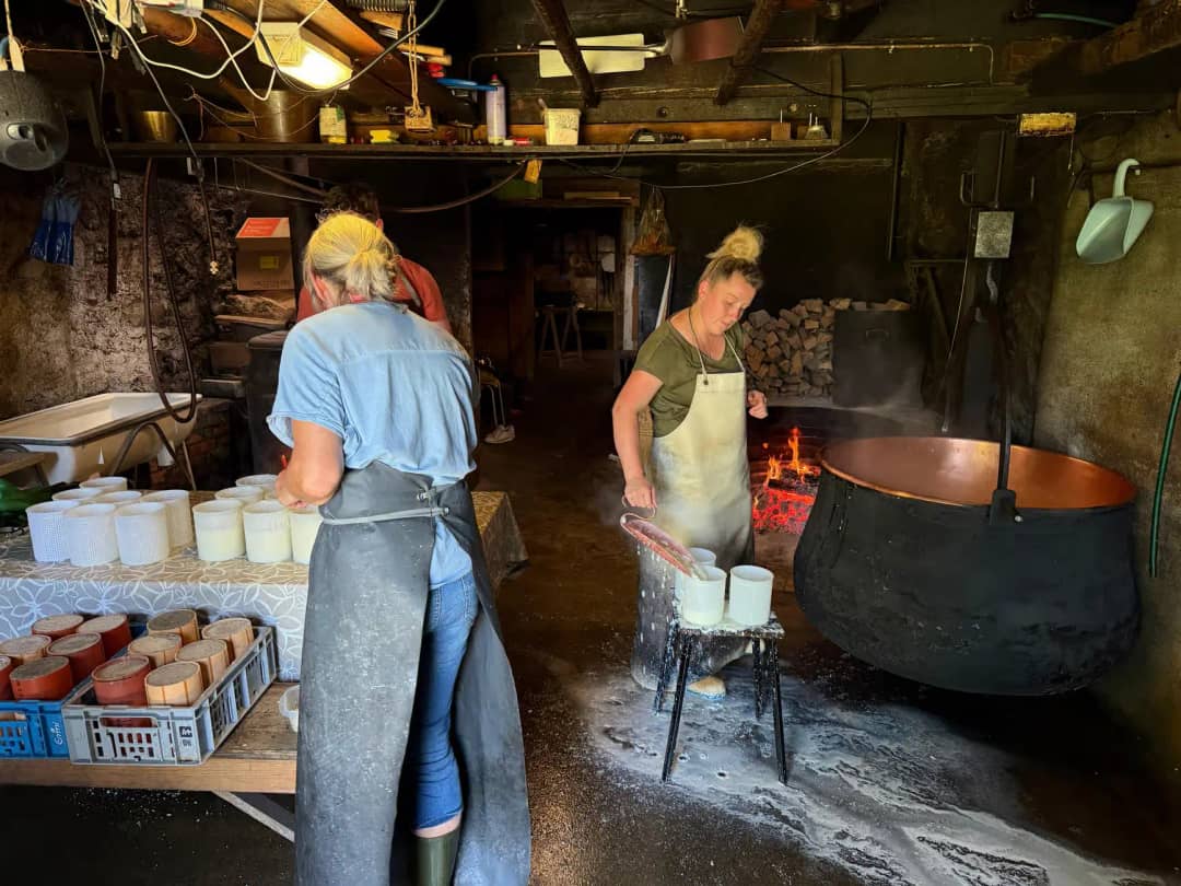 Daniela filling cheese moulds beside the copper cauldron over the wood fire, the demonstration kids watch on the farm tour