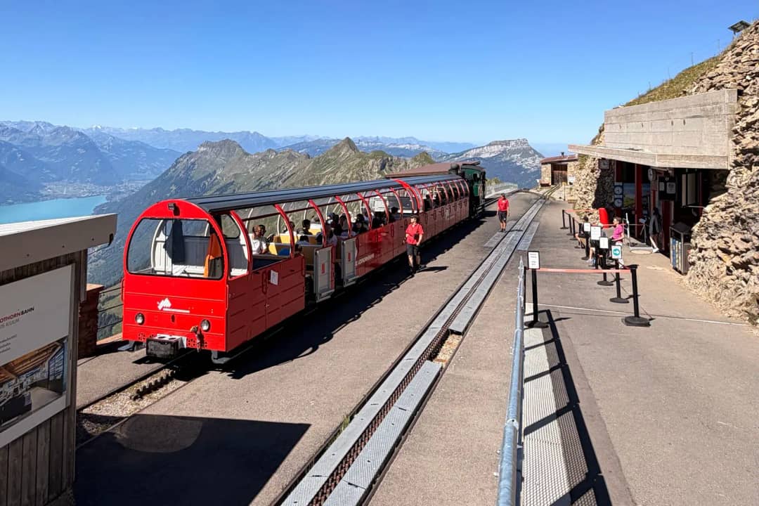 Rote offene Wagen und grüne Dampflok der Brienz-Rothorn-Bahn in der Bergstation hoch über dem Brienzersee