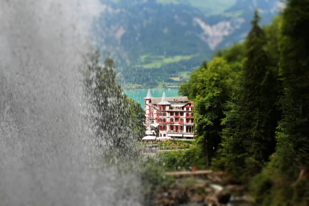 Le Grandhotel Giessbach vu à travers le rideau d'eau des chutes du Giessbach entre des pentes boisées