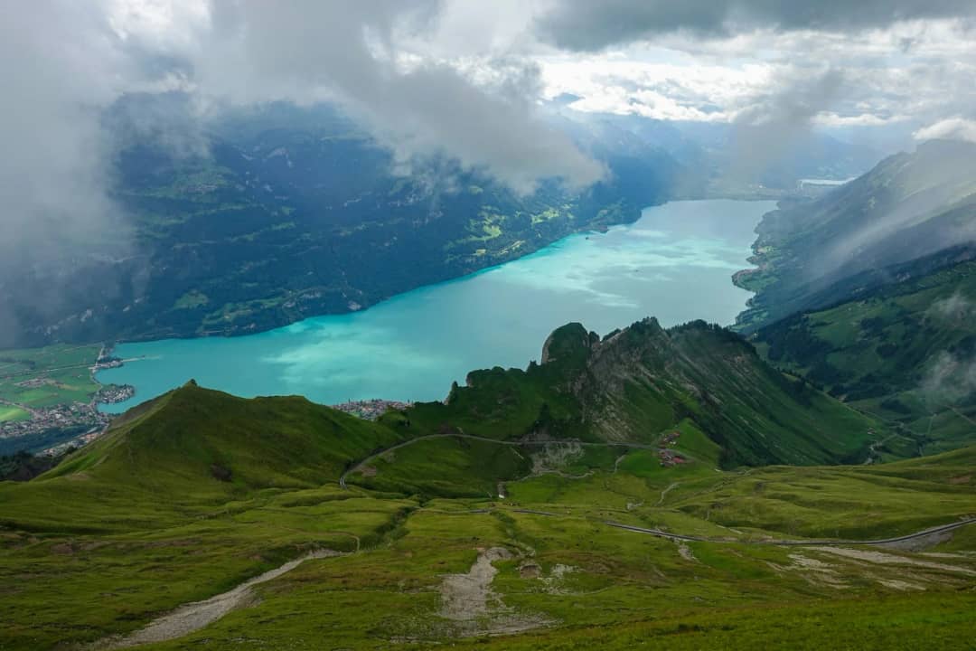 Cresta de hierba y sendero sobre el lago de Brienz turquesa, con nubes sobre las laderas lejanas