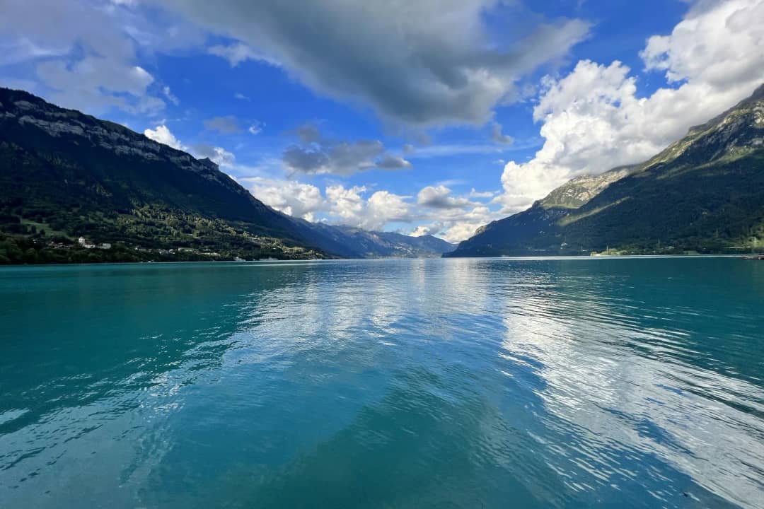 Ruhiger türkisfarbener See spiegelt weisse Wolken zwischen steilen, bewaldeten Bergen bis in die Ferne