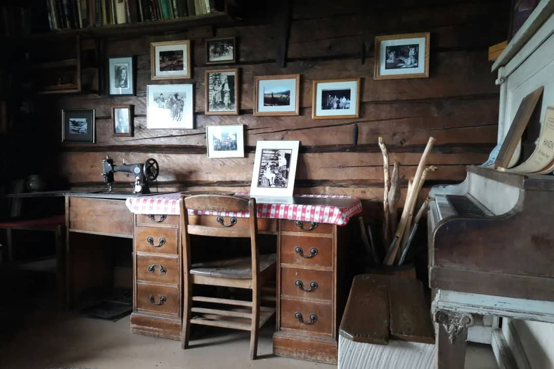 Wood panelled room with an antique writing desk, a wooden chair and old framed photographs on the wall