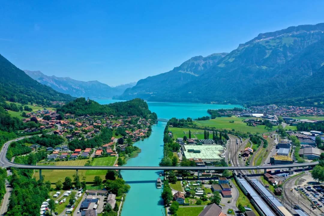 Luftaufnahme der Aare, die an Gleisen, Häusern und einem Campingplatz vorbei in den Brienzersee fliesst