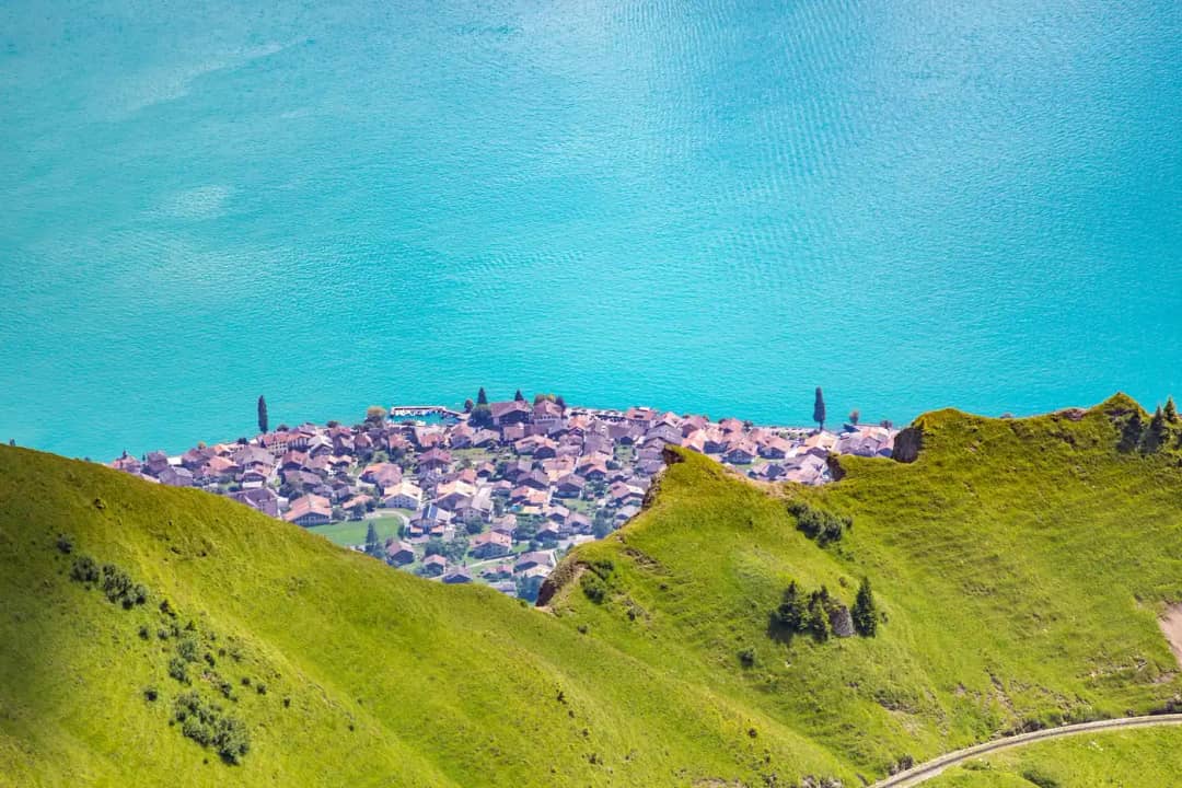 Ein Dorf am türkisfarbenen Ufer des Brienzersees, tief unten gesehen von den grünen Hängen des Berges