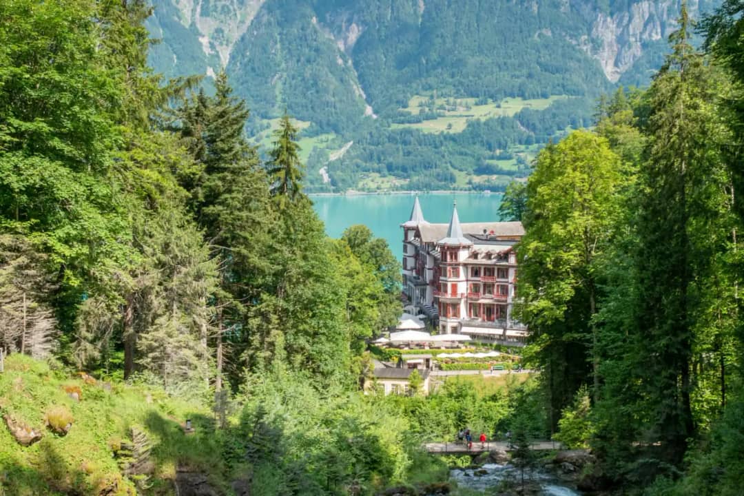 Grandhotel Giessbach framed by tall trees in the forest above the turquoise water of Lake Brienz in summer