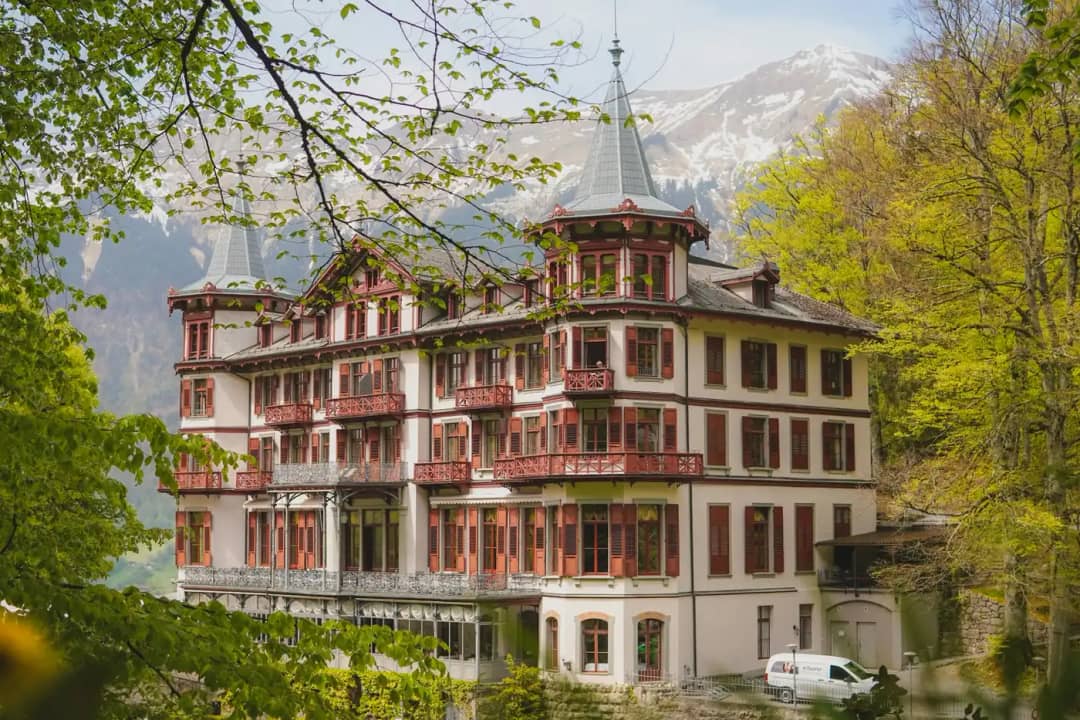 Façade rouge et blanche du Grandhotel Giessbach avec ses tourelles et balcons parmi les arbres au printemps