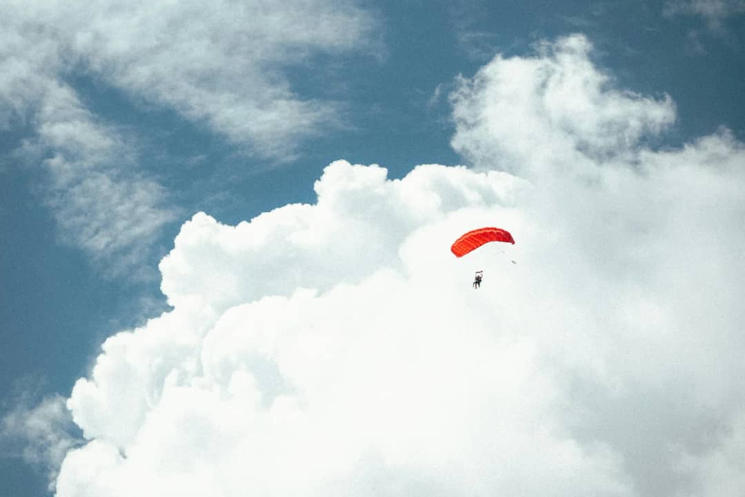 Kleiner roter Gleitschirm neben einer hoch aufragenden weissen Quellwolke am tiefblauen Sommerhimmel