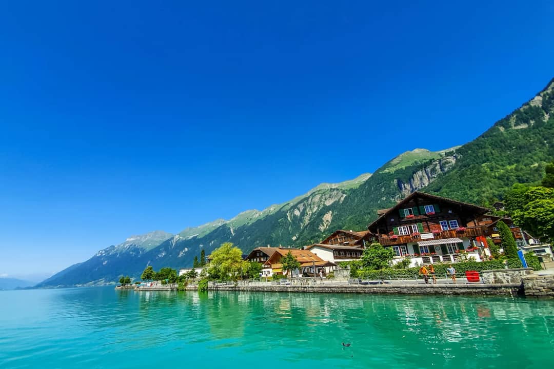 Chalets y un hotel a lo largo de la orilla turquesa bajo laderas verdes y un cielo azul intenso