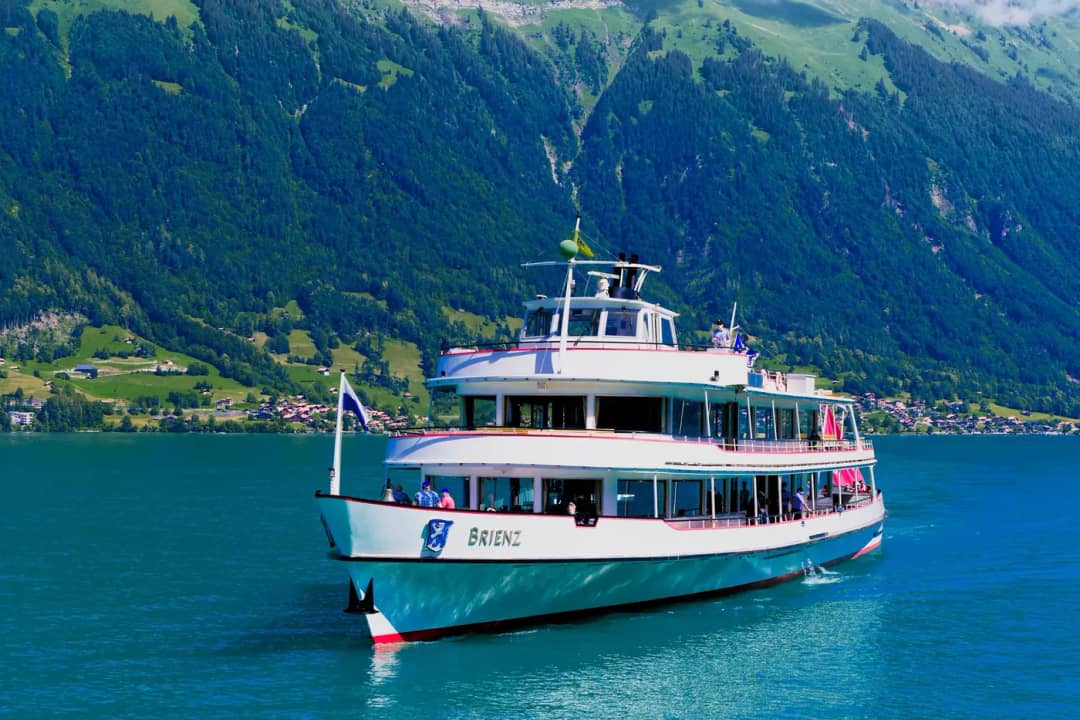 Das weisse Kursschiff MS Brienz fährt über das türkisfarbene Wasser des Brienzersees unter grünen Hängen