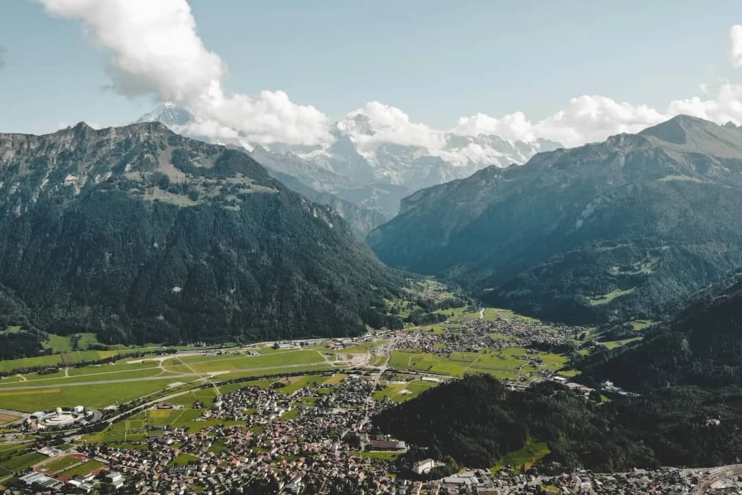 Interlaken und der grĂĽne Talboden zwischen steilen Bergen unter weissen Wolken, von einem Aussichtspunkt