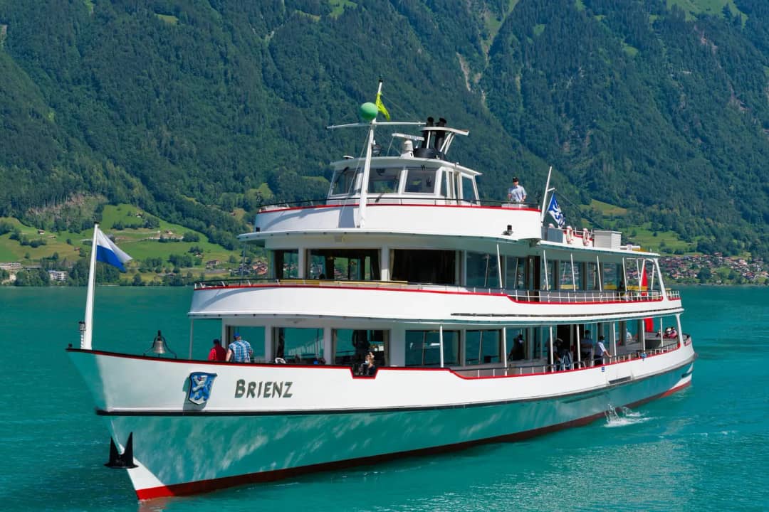 Le bateau MS Brienz, drapeaux au vent, traversant le lac de Brienz devant des pentes vertes et abruptes
