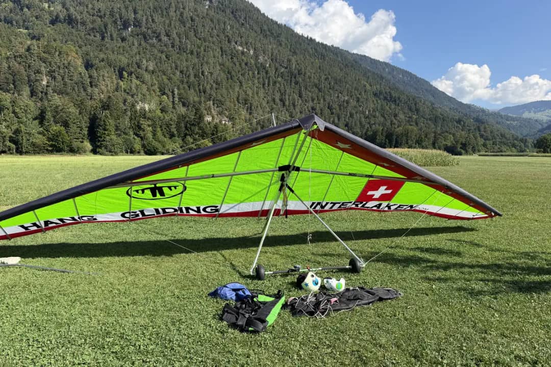 Tandem-Hängegleiter mit grünem Segel von Hang Gliding Interlaken auf einer Landewiese unter bewaldeten Bergen