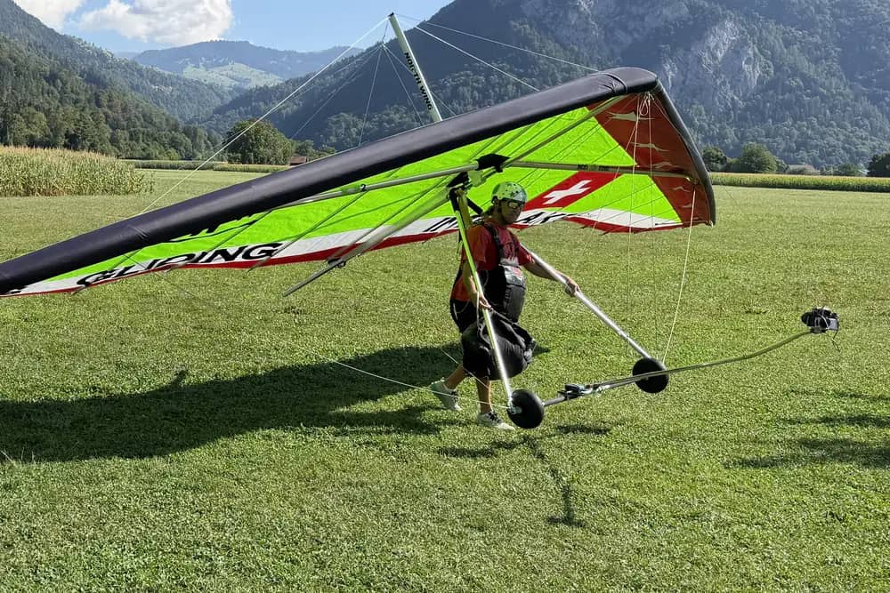 Tandempilot schiebt einen grünen Hängegleiter von Hang Gliding Interlaken auf Landerädern über die Wiese