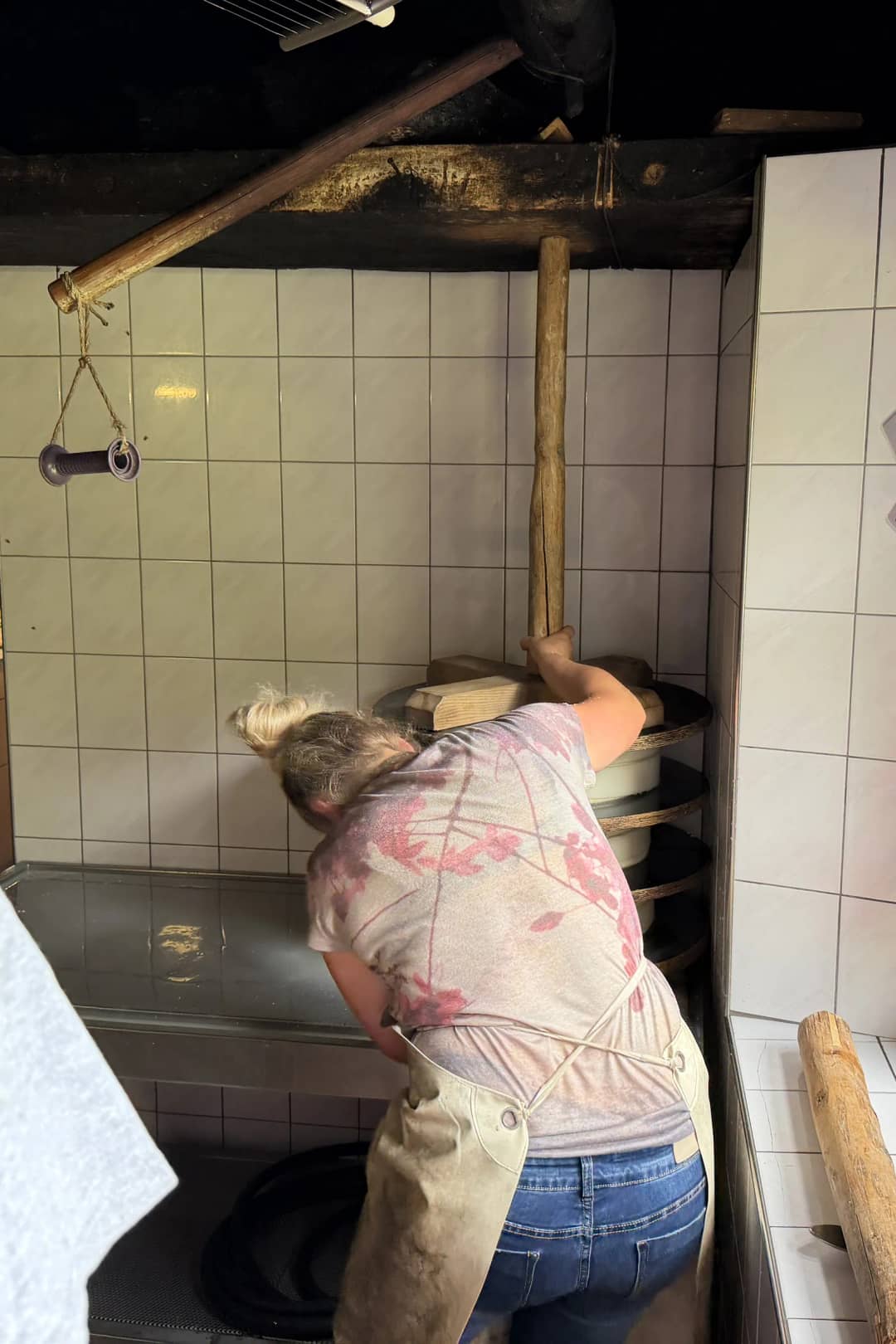 Fermière de dos au pressoir d'une petite fromagerie d'alpage carrelée, loin d'une fromagerie industrielle