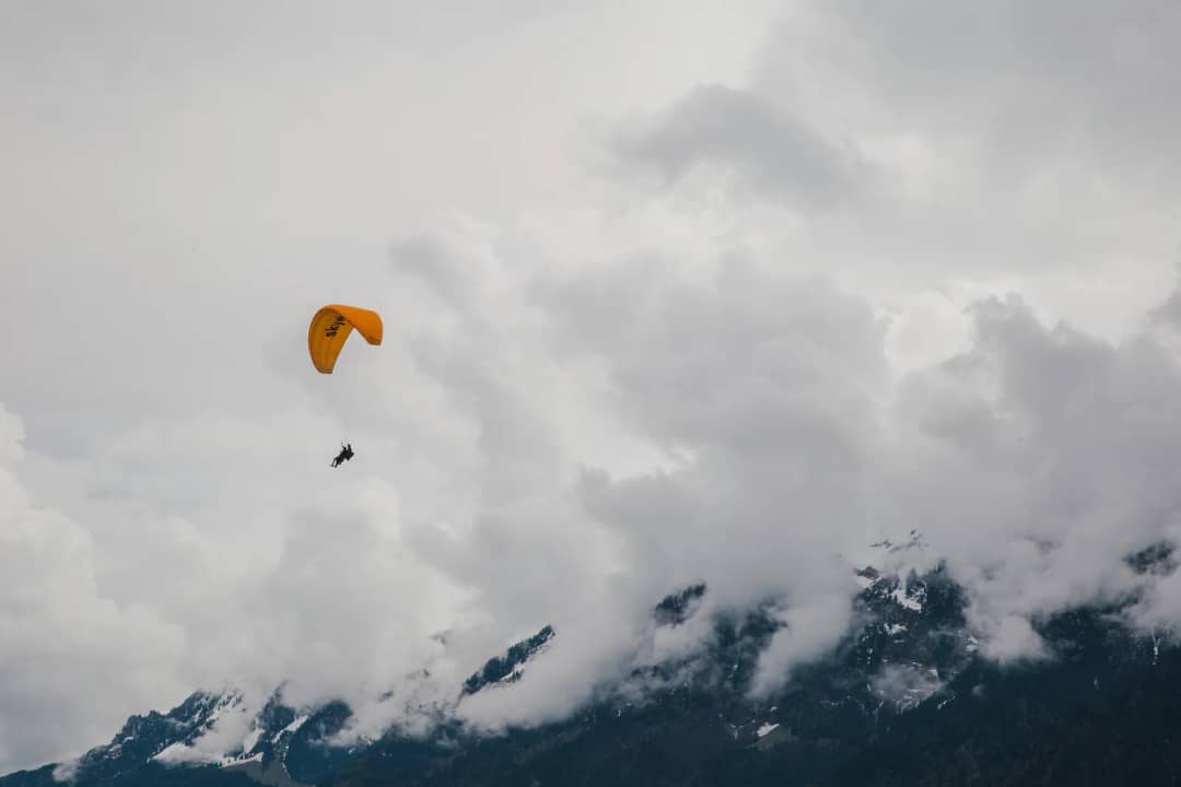 Parapente de ala amarilla entre nubes bajas, visto desde la pradera del Höhematte, donde aterrizan los pilotos