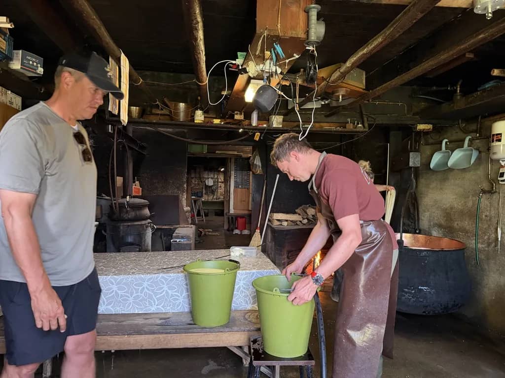 Visiteur debout près du jeune fromager et des seaux verts, sans la vitre d'une fromagerie de démonstration