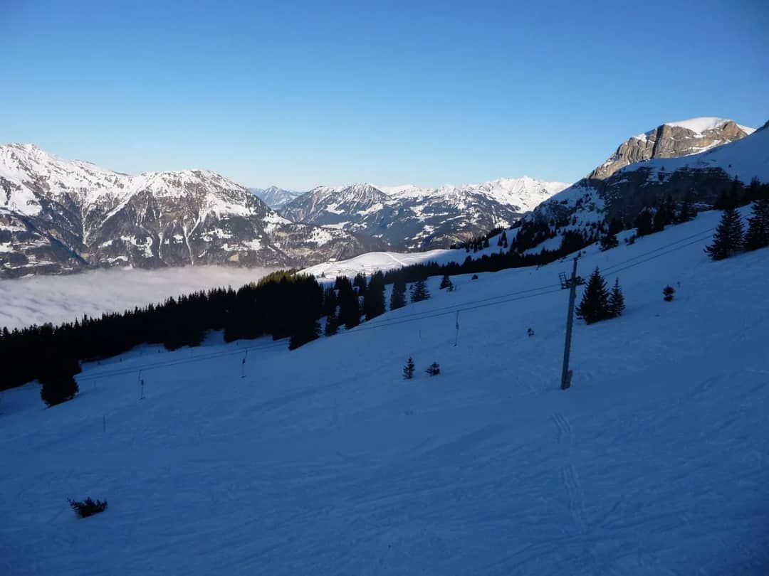 Verschneite Hänge des Wintersportgebiets Axalp über dem Nebelmeer, nahe dem Start des Schneeschuhtrails
