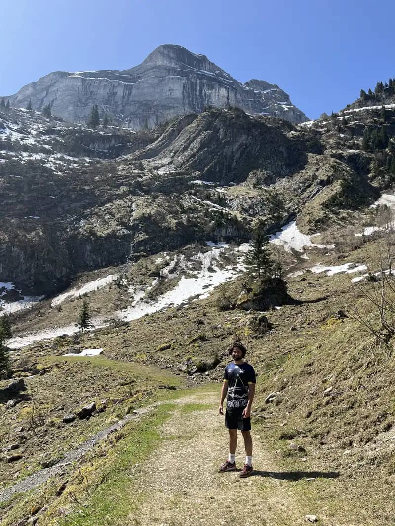 Wanderer auf dem Kiesweg von der Axalp zum Hinterburgseeli, dahinter Schneereste und steile Felswände