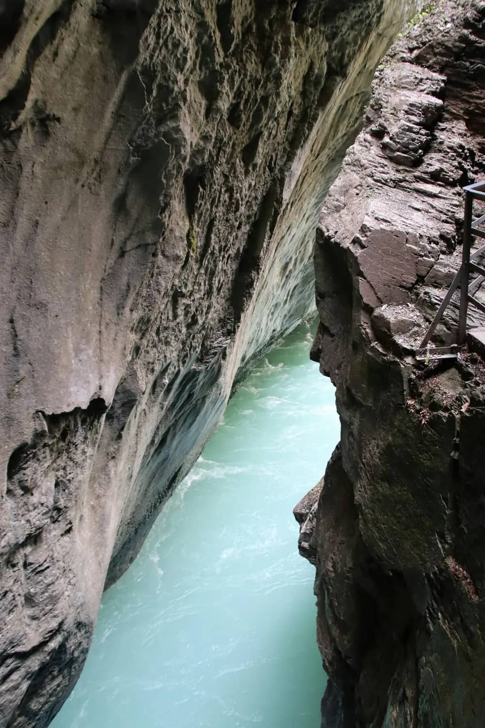 Milky turquoise Aare river squeezed between smooth grey limestone walls deep inside the Aare Gorge, Meiringen