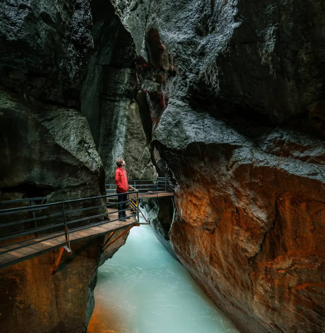 Walker in a red jacket at the railing of a rock tunnel above the pale turquoise water of the Aare Gorge