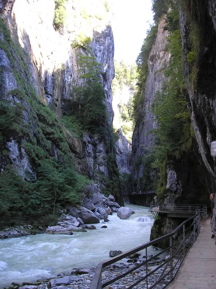 Wide view of the Aare Gorge with a wooden walkway along the right wall and the river rushing over pale stones