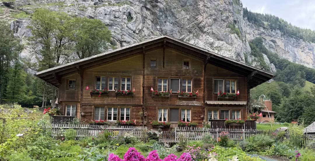 Chalé de madera con jardín florido en el fondo del valle de Lauterbrunnen, bajo el acantilado, en agosto