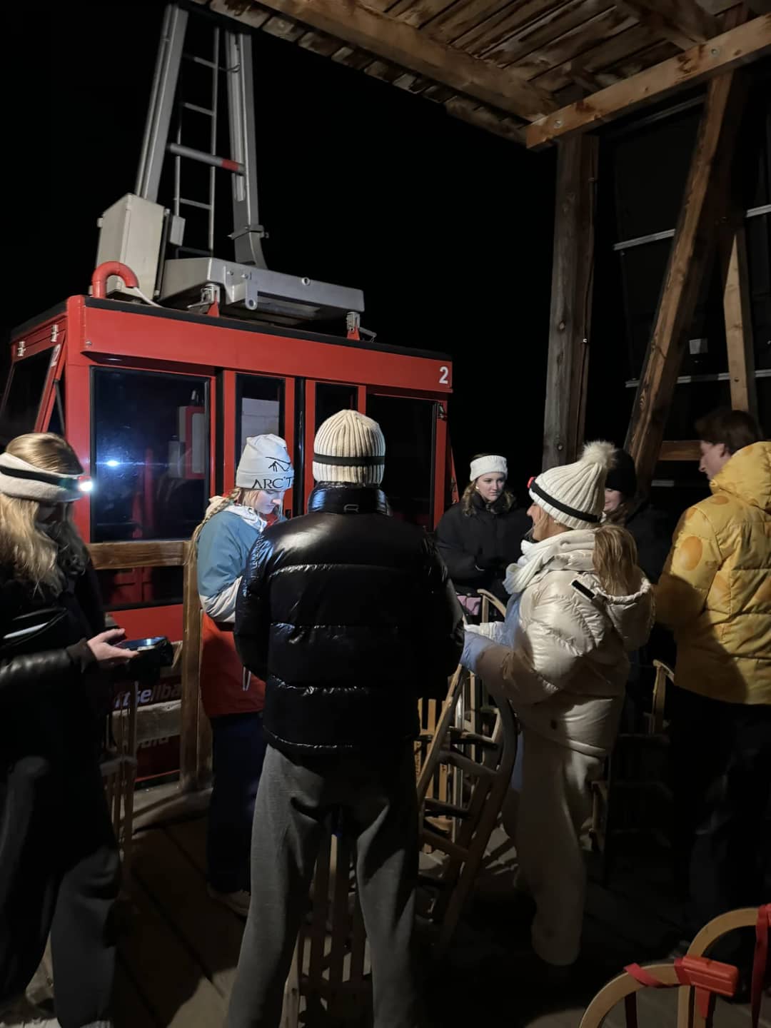A group with wooden sledges waiting at the Isenfluh Sulwald cable car on a winter evening above Lauterbrunnen
