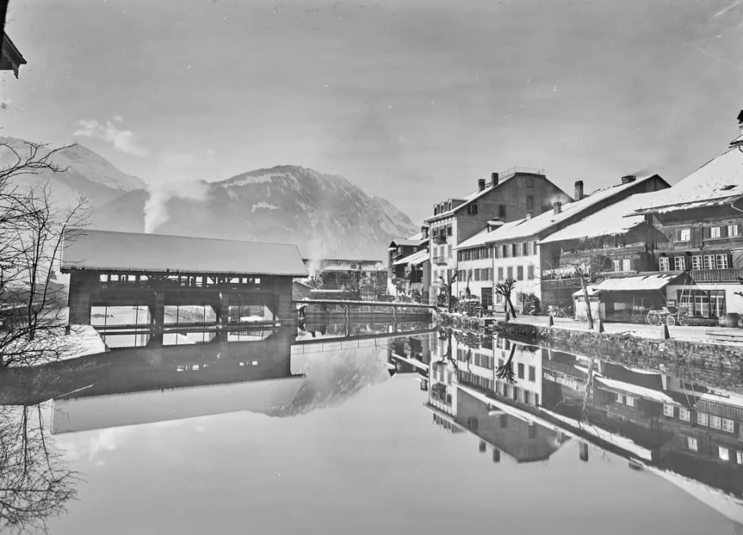 Día de invierno en el Aare en Unterseen en 1910, tejados nevados y puente cubierto reflejado en el río
