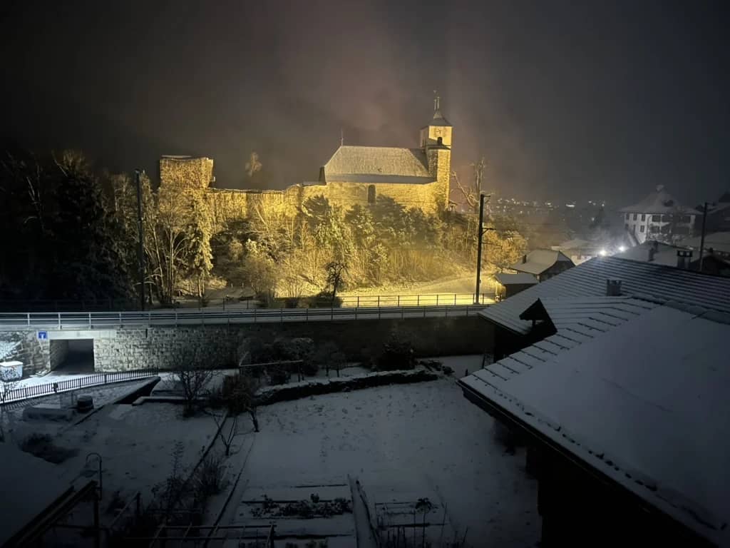 Iglesia de Ringgenberg en su colina con nieve fresca de noche en diciembre, iluminada sobre el lago de Brienz
