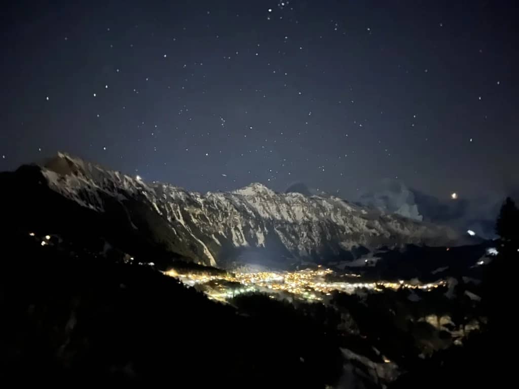 Luces del pueblo abajo, bajo montañas oscuras y nevadas, cielo estrellado de diciembre, vistas desde Isenfluh