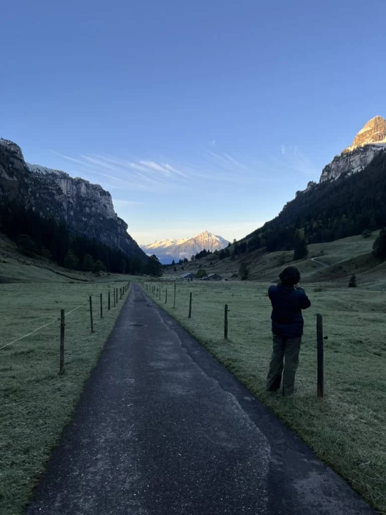 Un caminante en el camino del Justistal al amanecer a finales de septiembre, con prismáticos hacia la ladera