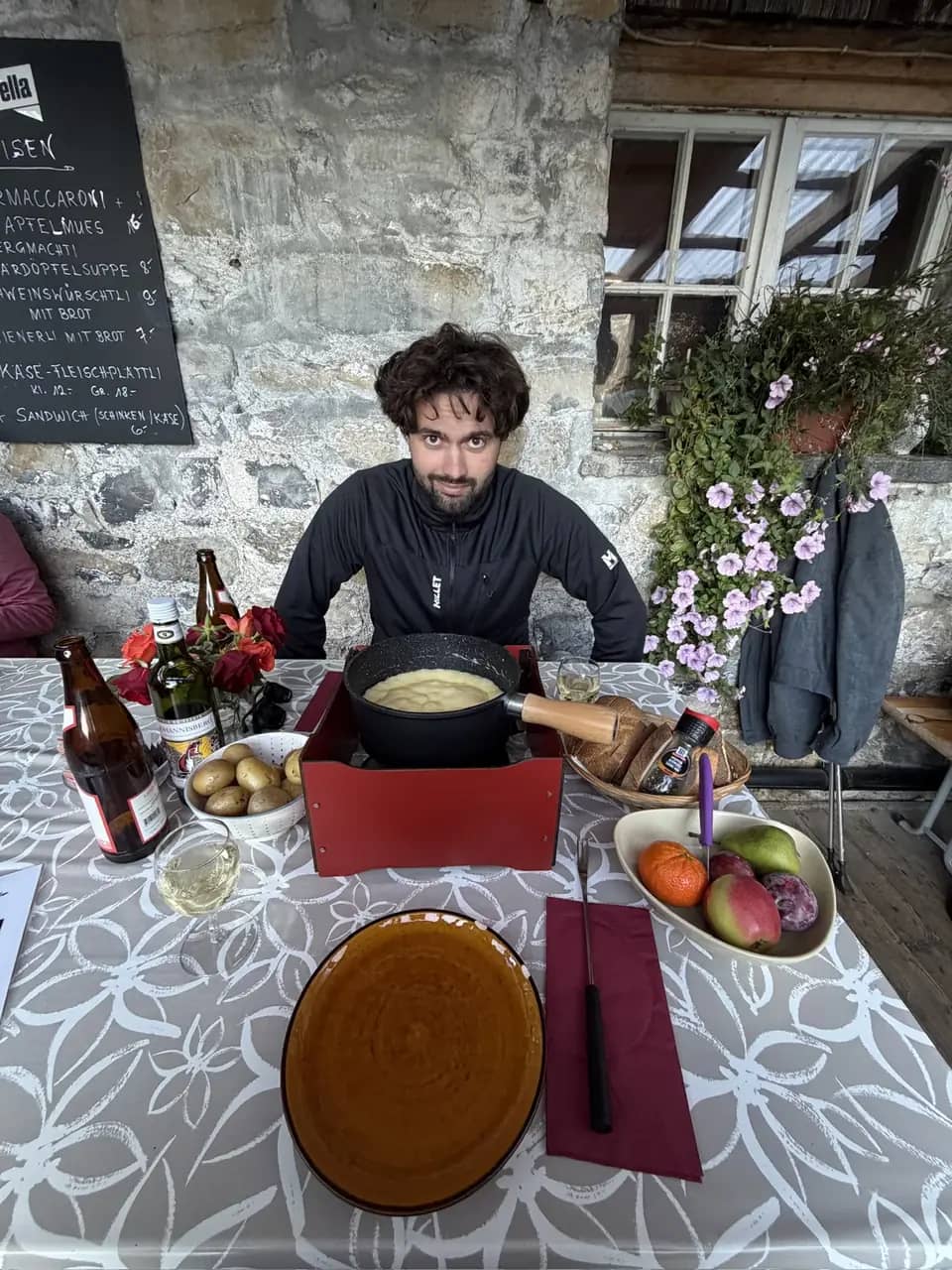 Una fondue de queso en una terraza cubierta de una granja del Justistal, un guía sentado a la mesa