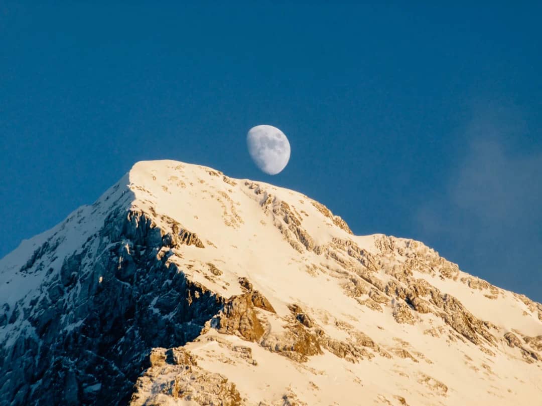 La cumbre nevada del Eiger iluminada por el sol de una tarde de invierno, con la luna en un cielo azul intenso