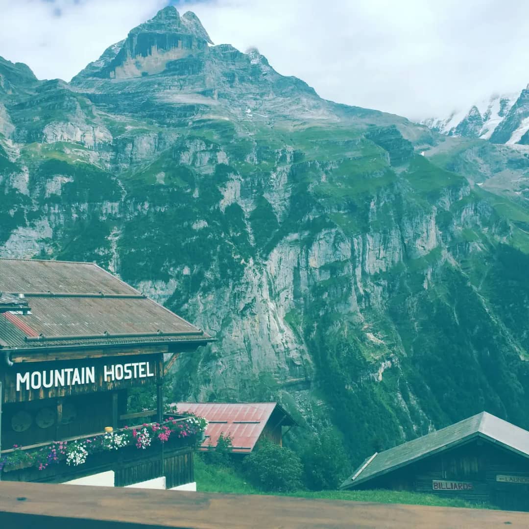 Enseigne du Mountain Hostel à Gimmelwald avec balcon fleuri, vieilles granges et falaises de Lauterbrunnen
