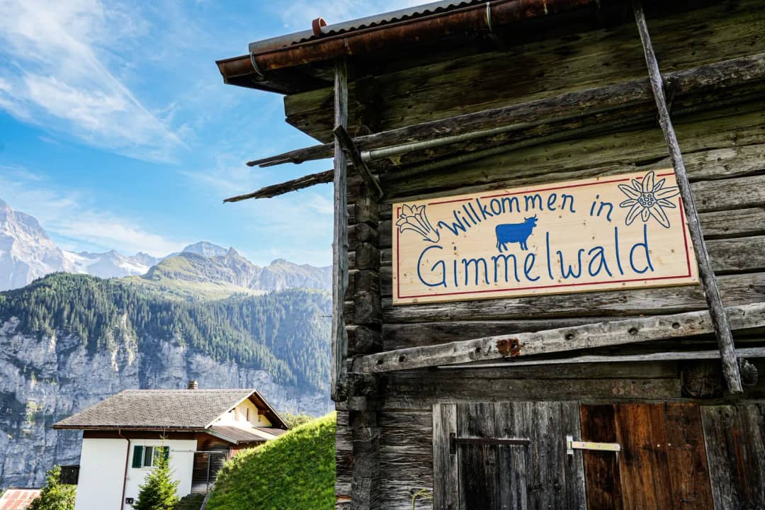 Panneau « Willkommen in Gimmelwald » sur une grange au-dessus d'un chalet et des falaises de Lauterbrunnen