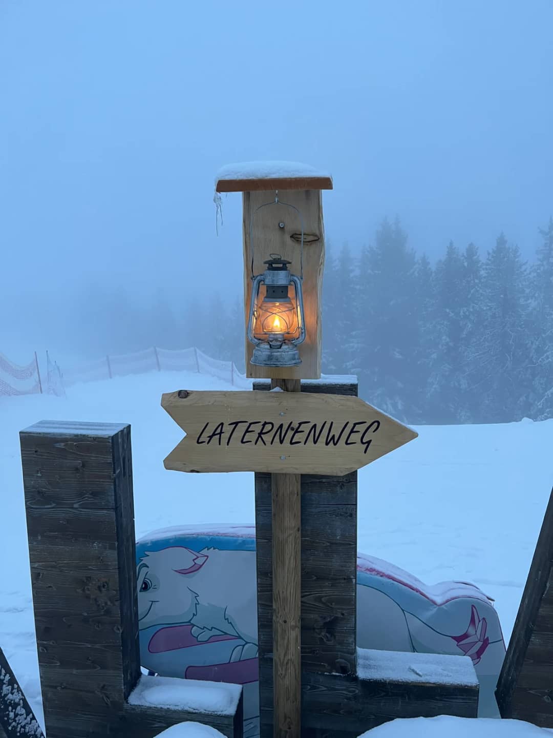 Laternenweg signpost and a glowing lantern in thick fog above Mürren, no mountains visible, a cloudy day