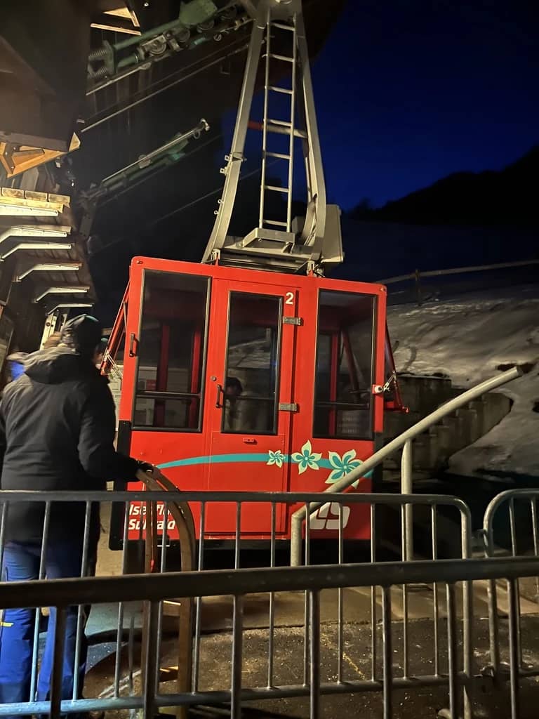The small red cabin of the Isenfluh-Sulwald cable car waits at the lit valley station on a winter evening